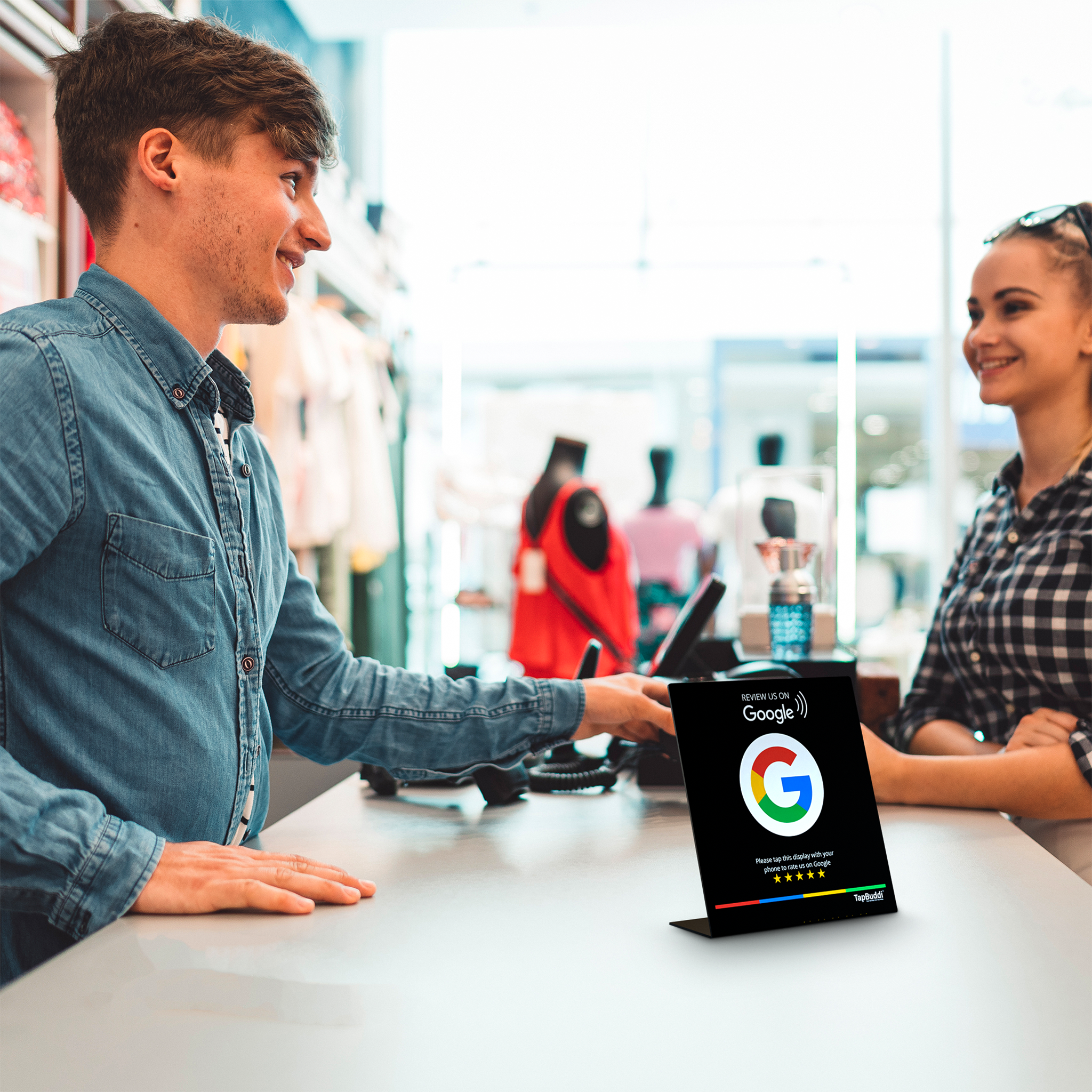 Klant aan de balie van een winkel naast een zwart Google review display van TapBuddi